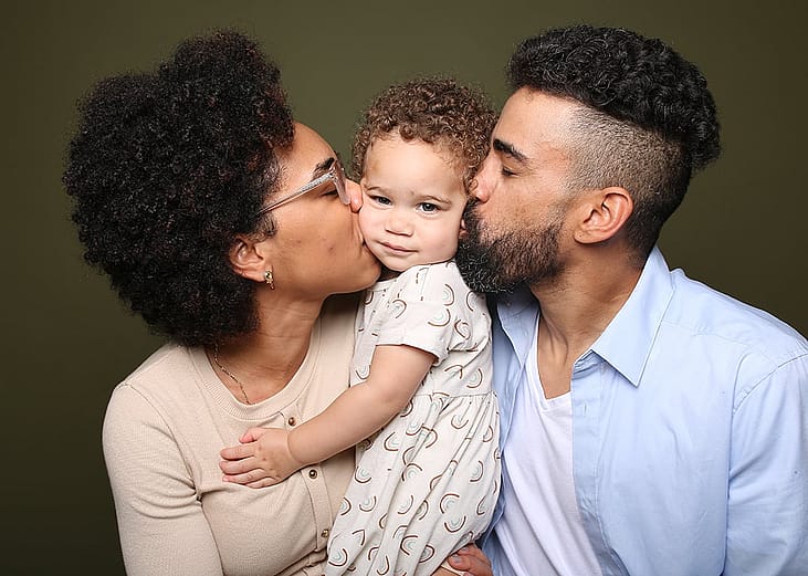 A mother and a father kissing their baby's face.