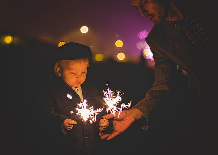 A father helping his young child with sparklers during a New Year celebration.