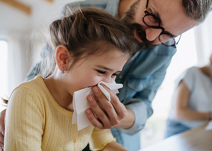 A father helping his young daughter to blow her nose.