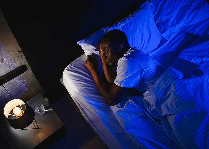 A person enjoying a night's sleep under his bed's linen sheets.