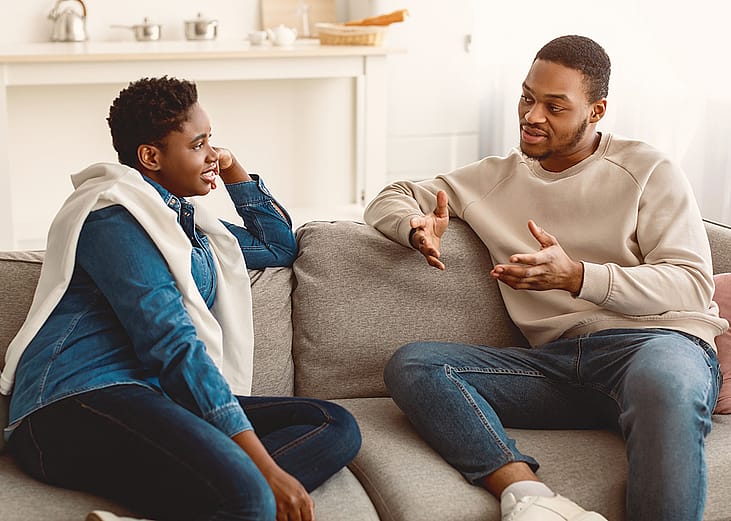 A couple sitting on the couch at home and having a serious conversation.