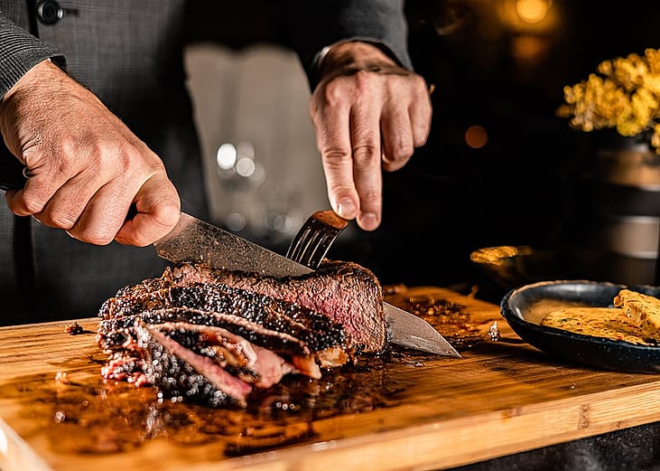 A butcher slicing a tomahawk steak in a serving table for a customer in a steakhouse restaurant.