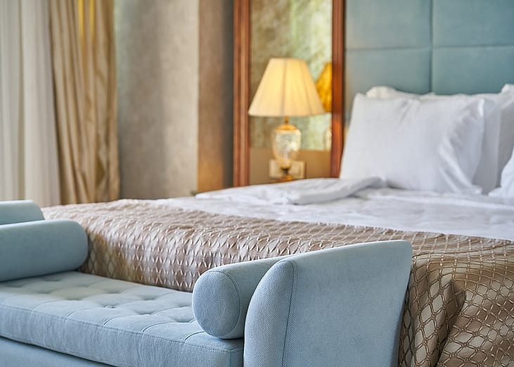 A premium bed, sofa, and bedside furniture inside a luxurious hotel room.