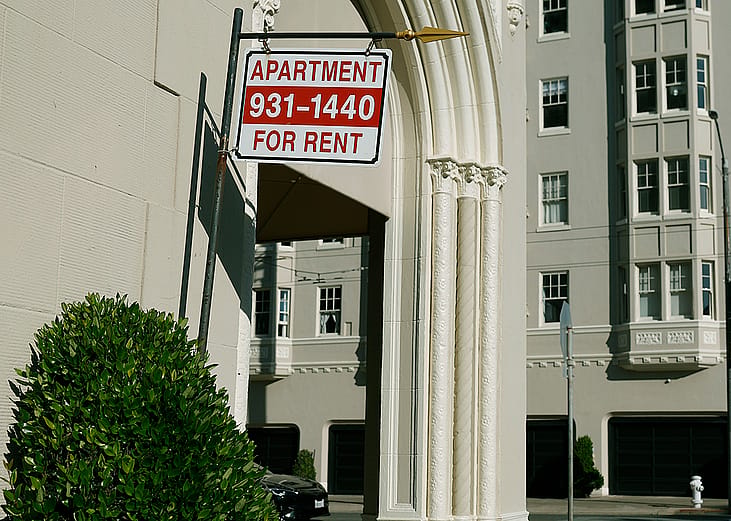An 'apartment for rent' sign hangs outside of an apartment building.