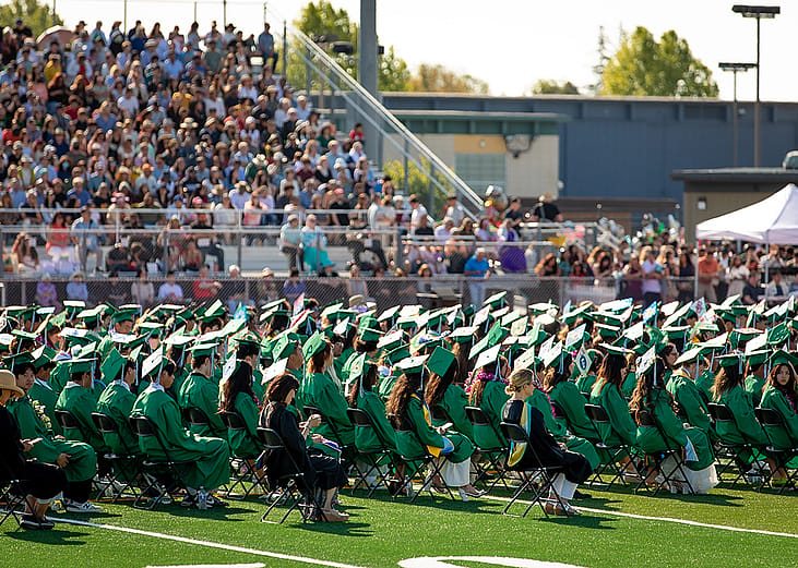  A high school graduation ceremony happening outdoors in the campus' sports field.