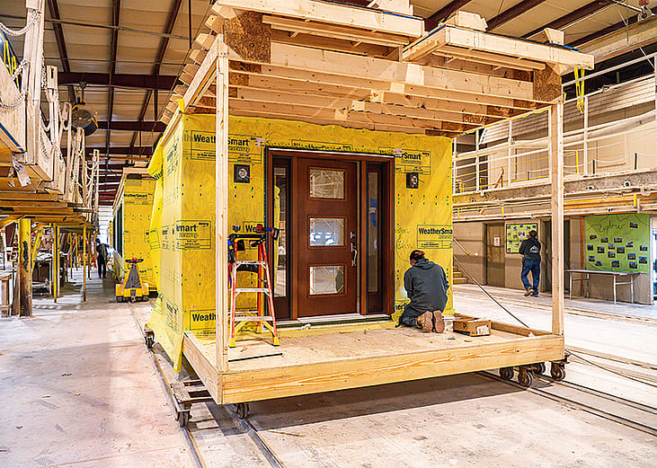 A worker kneels on a wooden platform building a modular home under construction in a factory in Middleburg, Pennsylvania.