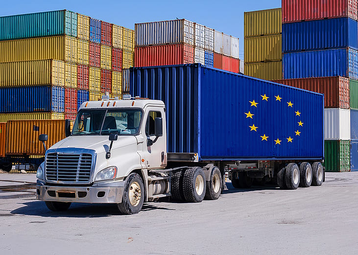 A truck in a shipyard with an EU-marked shipping container.