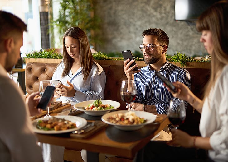 A group of business colleagues checking their smartphones while eating lunch in a restaurant.