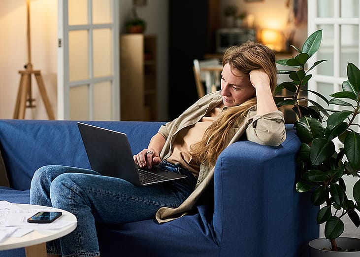 A stressed young woman at home looking at taxes from a laptop.