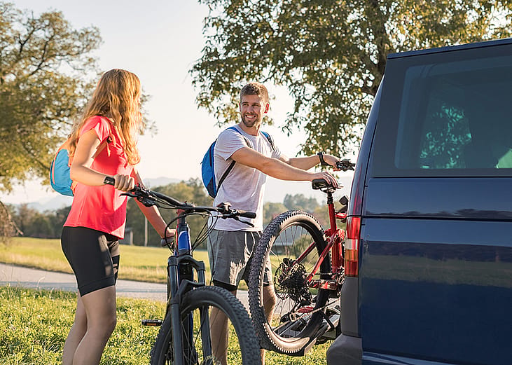 A couple taking down electric mountain bikes from their van for a nature recreational adventure.