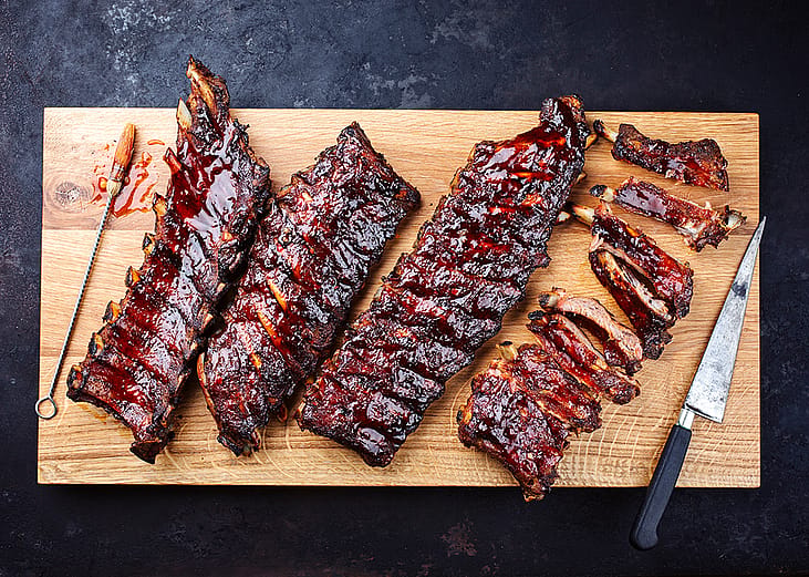 Slabs of freshly barbecued ribs sliced on a wooden cutting board.