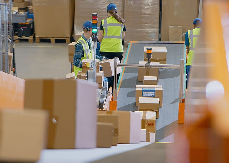 A logistics team in a warehouse working along a conveyor belt to sort and load packages.