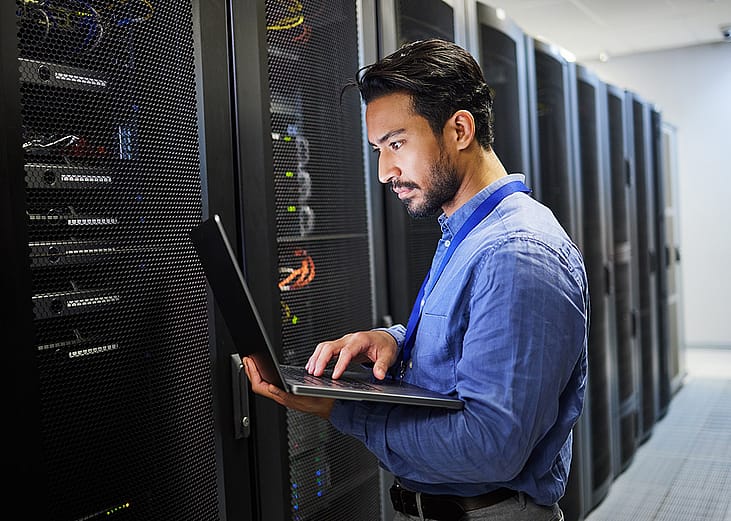 A programmer working on a laptop for maintenance and network server checking in a data center.