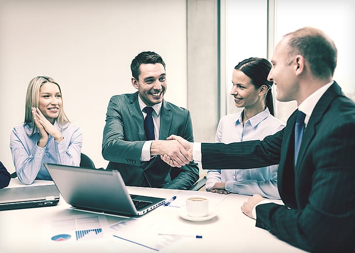 A business team with its two leaders shaking hands during a meeting.