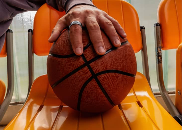 A player's hand wearing an Oura ring placed over a basketball.