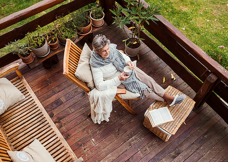 Top view of an elderly woman with a book while sitting relaxingly by her home's terrace.