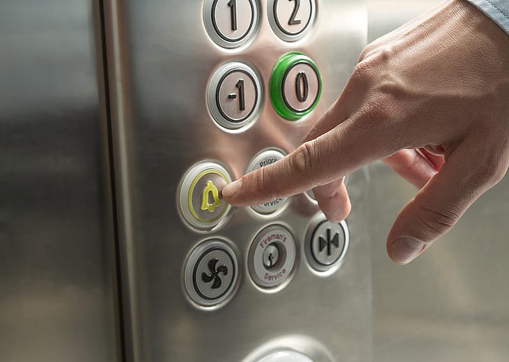 A person's hand pressing the alarm button in the elevator.