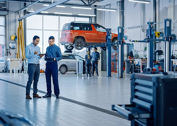 A manager explaining diagnostics results and vehicle breakdown to a mechanic in a car workshop.