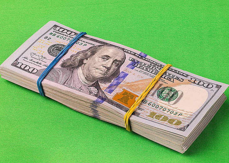 A pack of 10,000 U.S. dollars laid on a striking green background.
