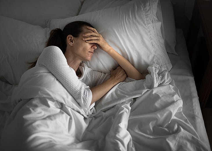 A tired woman in bed struggling to sleep.