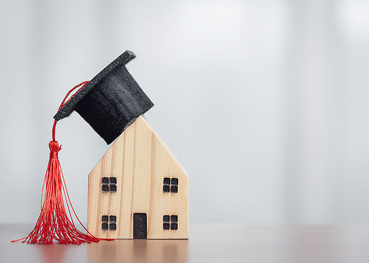 A miniature figures of a graduation cap on a wooden house, symbolizing the concept of success in education.