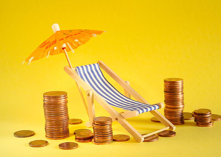 Coins around a beach deck chair and umbrella as a concept of saving for a holiday.