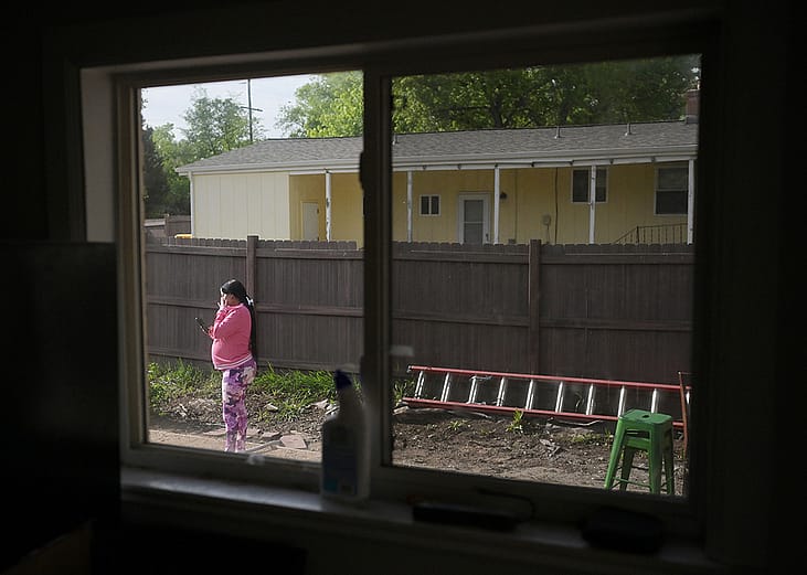 A pregnant woman standing in the backyard of her rental home in Denver, USA while using a smartphone to call her husband in Venezuela.