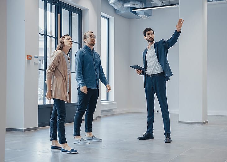A real estate agent showing an empty office space for rent to clients.
