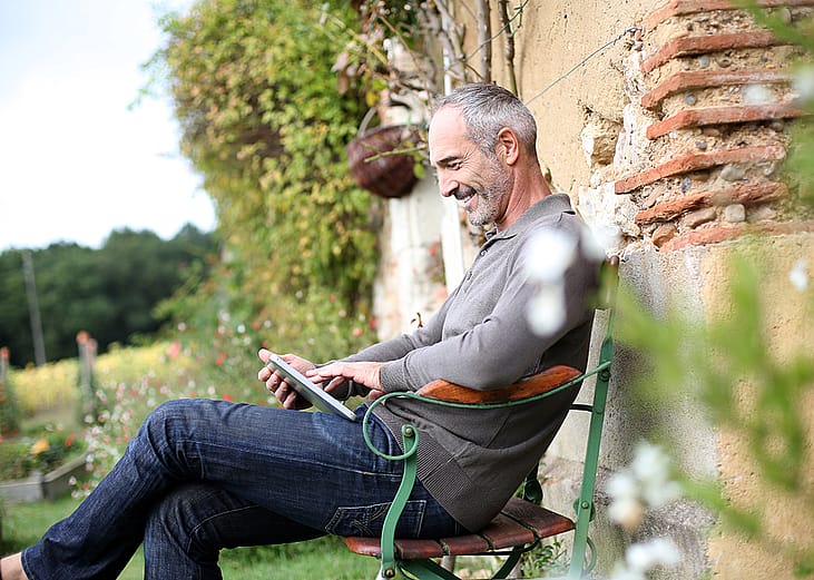 A middle-aged man using phone while sitting on a bench in a countryside home.