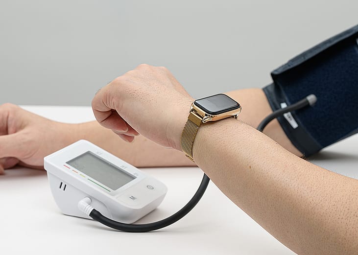 A person measuring blood pressure using a digital device and a smartwatch.