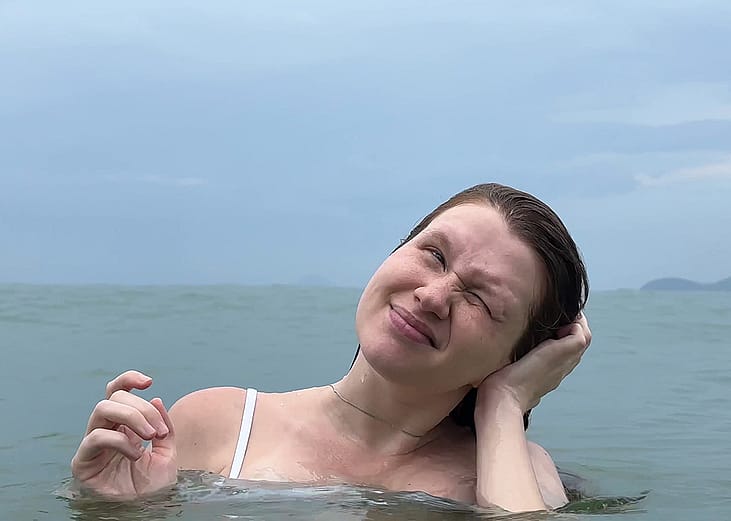 A person tilting her head sideways to remove water from her ear after swimming.