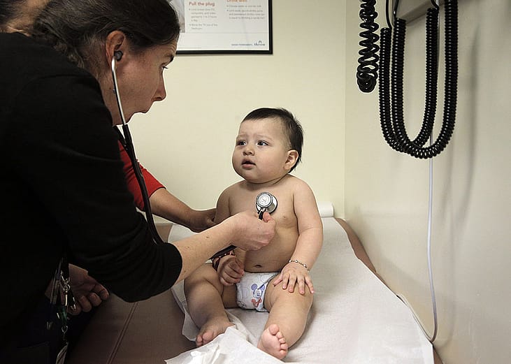 A pediatrician distracts a 9-month-old boy to check his heartbeat.