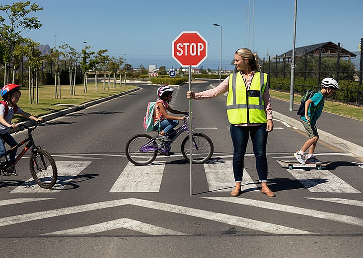 A female traffic enforcer helping school children riding bicycles cross the road.
