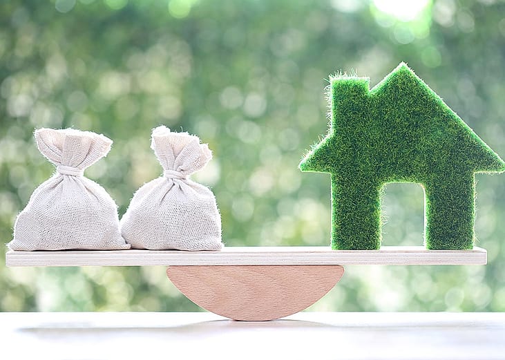 A bag of money and a figure of a home on both ends of a seesaw as a concept of weighing finances and home equity.