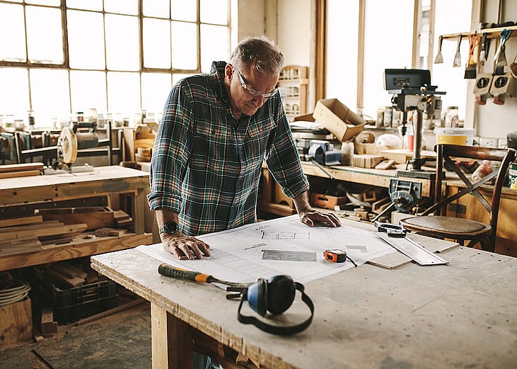 A senior carpenter studying sketches before starting work at his workshop.
