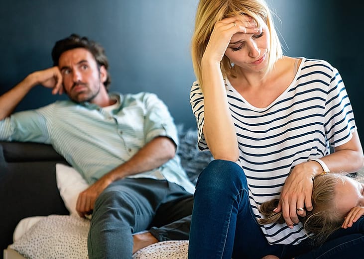 A stressed couple sitting in their living room while the mother comforts her young child.