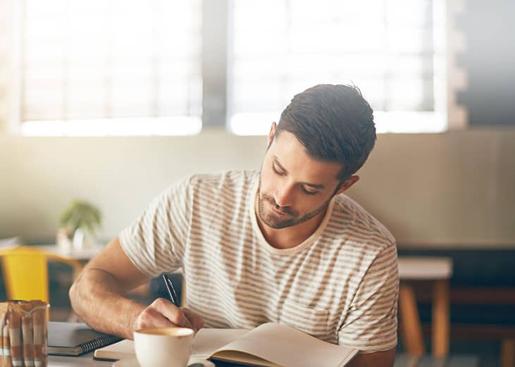 A man spending a slow down time and journaling in his notebook at a cafe.
