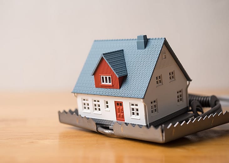 A miniature house within a mouse trap placed in a wooden table.