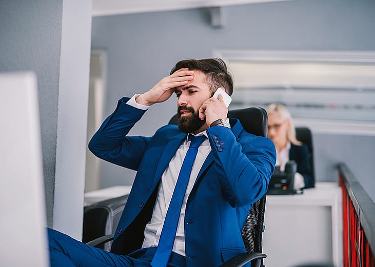 A business manager appearing to be frustrated during a phone call with a client. 