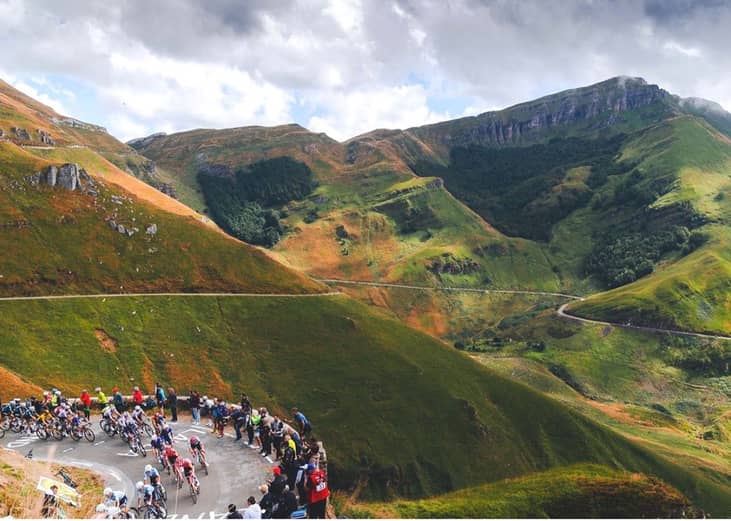 Cyclists descending from a mountain route, with spectators lining up the steep to watch them.