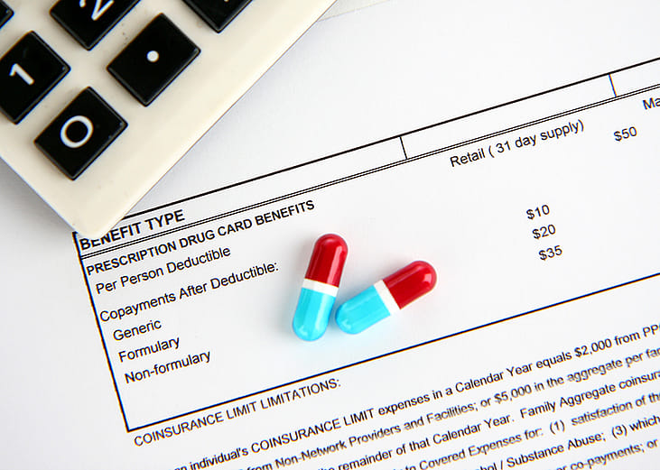 Two medicine pills and a calculator placed above a medical statement.