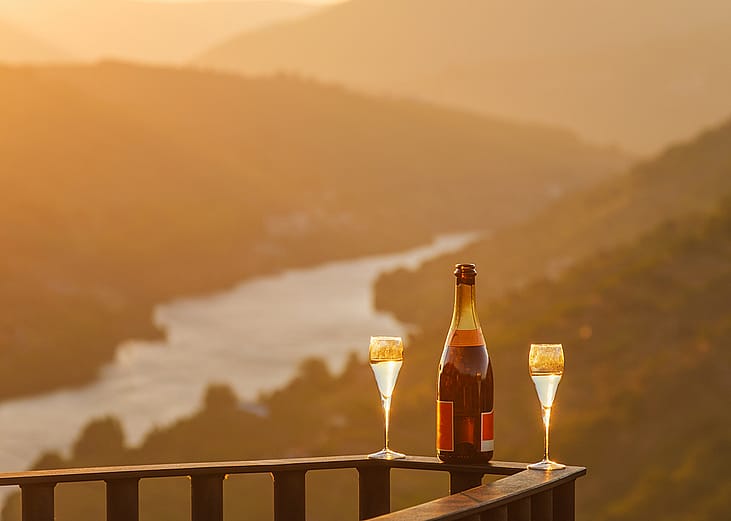 A bottle of wine and two glasses on a balcony rail with the view of the Douro Valley in Portugal.