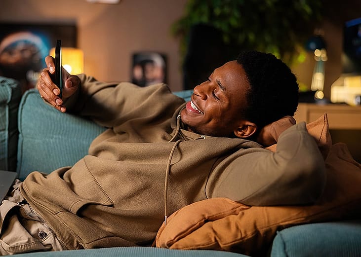 A young man happily checking information on his phone while relaxing at home.