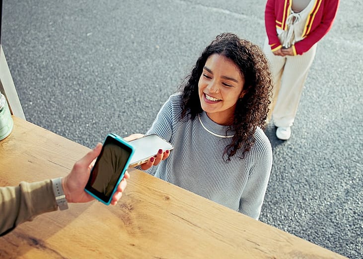 A young woman paying for her food at a food truck using cashless phone payment.