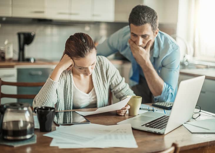 An upset couple paying bills and debt online from a laptop at their home.