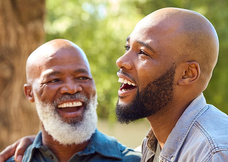 A senior father with his adult son happily engaged in a conversation outdoors.