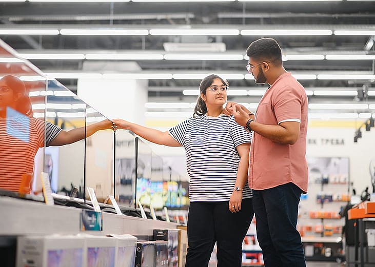 A young couple at an appliance store contemplating to buy a new flatscreen TV.