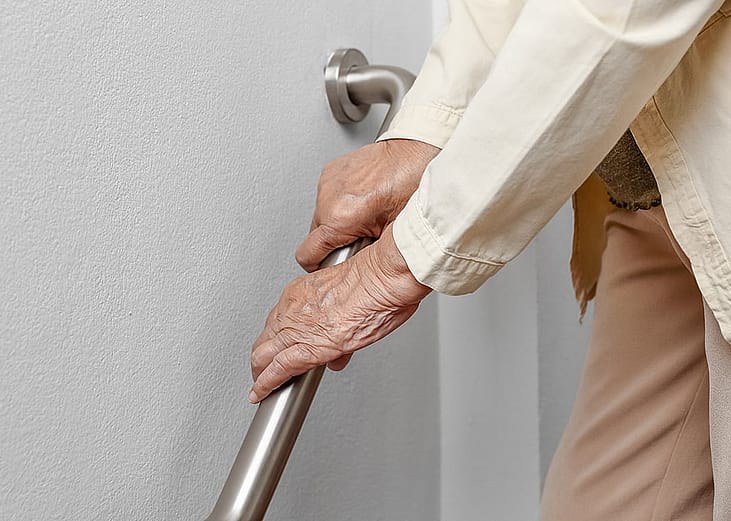 A senior woman holding onto a handrail to safely walk down the stairs.