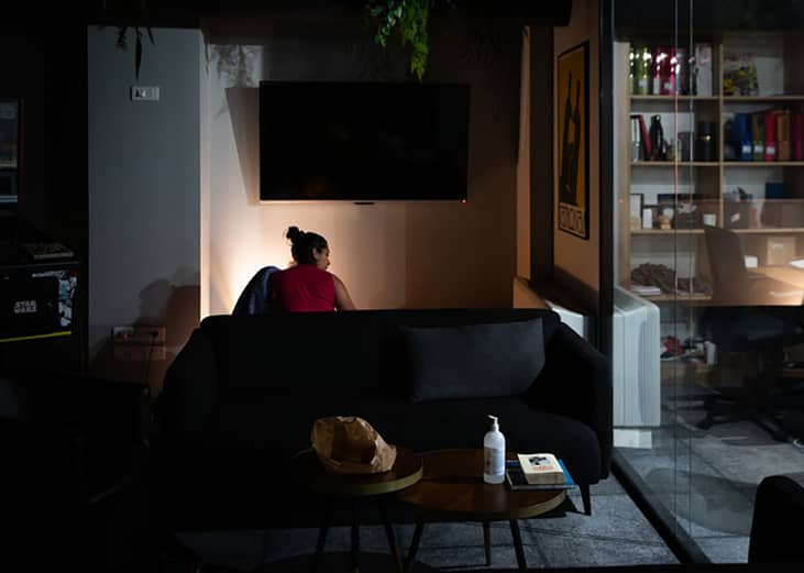 A young woman settling in at night to sleep at an office space's sofa.