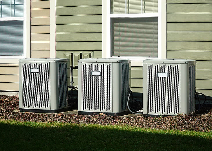 Three air conditioner compressor units placed behind a house.